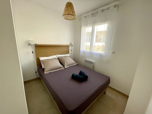 Camera accogliente della Résidence Marina di Bravone a Linguizzetta con letto in legno, lenzuola viola e porte con vista sul mare