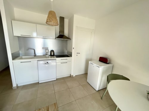 Moderna zona cucina-soggiorno in appartamento T3 a Résidence Marina di Bravone, Linguizzetta con mobili bianchi e acciaio inossidabile