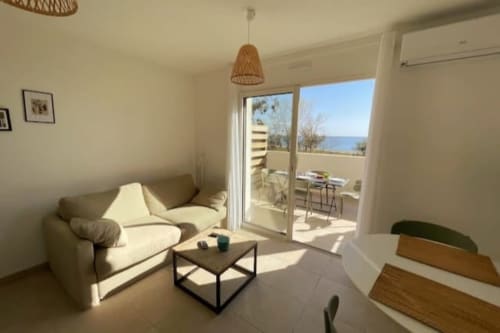 Luminoso appartamento a Marina di Bravone con divano color crema, balcone con vista mare, lampada sospesa in vimini e arredi moderni
