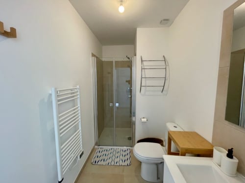 Salle de bains moderne de la Résidence Marina di Bravone avec douche, toilettes, lavabo, porte-serviettes chauffant et accessoires en bois
