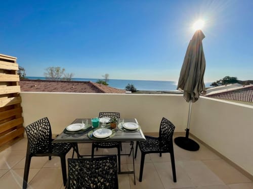 Terrasse avec vue sur mer à la Résidence Marina di Bravone : table à manger, chaises et parasol face au littoral corse