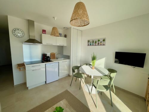 Cuisine ouverte et salle à manger contemporaines à la Résidence Marina di Bravone avec mobilier blanc, suspensions en rotin et table ronde