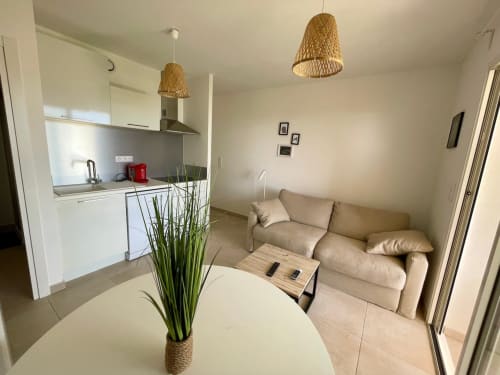 Appartement T3 moderne à la Résidence Marina di Bravone avec cuisine ouverte, canapé beige, table ronde et suspension tissée