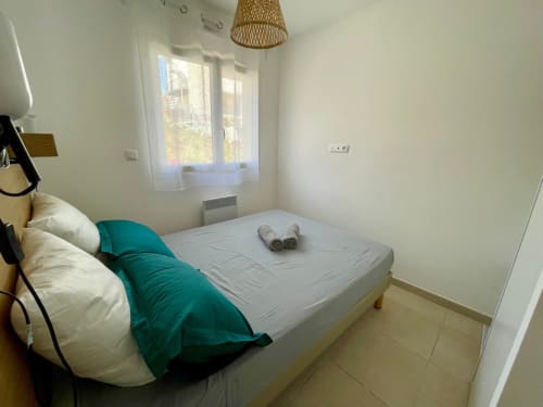 Chambre moderne à la Résidence Marina di Bravone avec accents bleu-vert, baie vitrée vue mer et mobilier contemporain