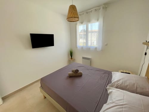 Modern bedroom at Résidence Marina di Bravone in Linguizzetta with bed, wall-mounted TV, wicker pendant light, and sea-view