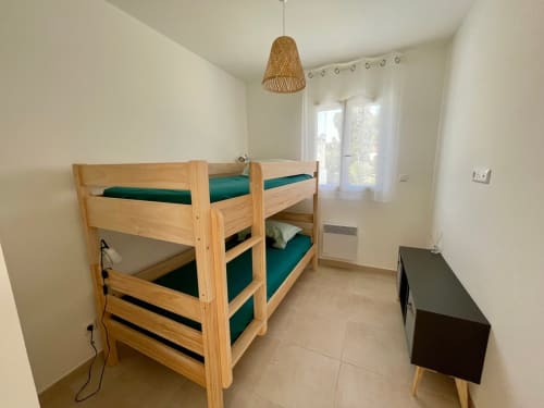 Bright bedroom at Marina di Bravone with wooden bunk beds, green mattresses, and wicker pendant light in Linguizzetta