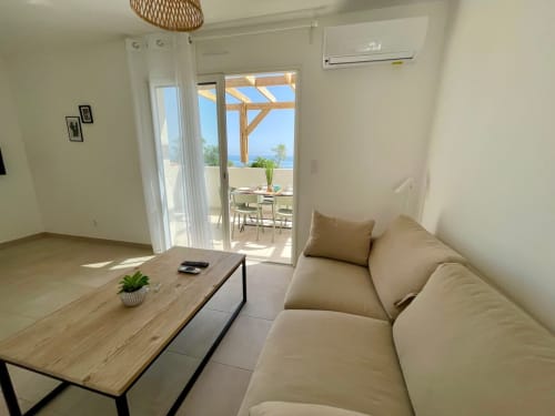 Modern apartment living room at Marina di Bravone with beige sofa, wooden table, sea view terrace, and air conditioning