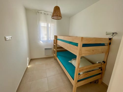 Bright bedroom in Résidence Marina di Bravone with wooden bunk bed, turquoise bedding, modern fixtures and beach access in