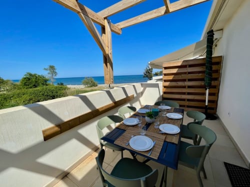 Beachfront terrace at Résidence Marina di Bravone with dining table, lounge seating, wooden pergola overlooking Mediterranean