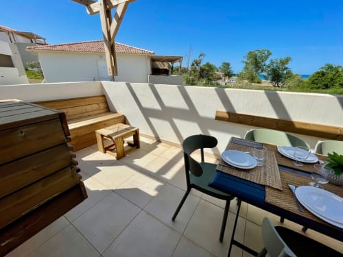 Seaside terrace at Résidence Marina di Bravone with dining table, wooden benches, and sea views in Linguizzetta