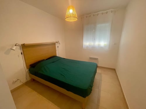 Chambre avec lit en bois, parure de lit verte, suspension en fibres tressées et fenêtre à l'hôtel Marina di Bravone, Linguizzetta
