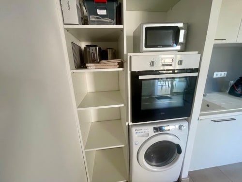 Cuisine moderne de l'appartement Résidence Marina di Bravone avec micro-ondes, four, lave-linge et étagères blanches.