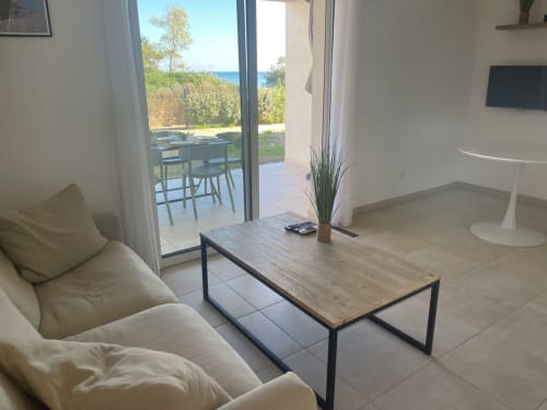 Séjour moderne à la Résidence Marina di Bravone avec vue mer, canapé beige, table en bois et accès à la terrasse