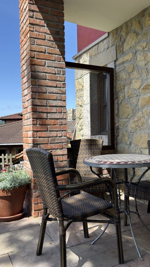 Zona de estar exterior en los apartamentos rurales El Picoretu con chimenea de ladrillo y muros de piedra en Mestas de Con