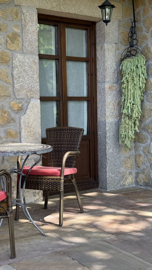 Stone patio at El Picoretu rural apartments with wicker chair, table, hanging plant, and wooden door overlooking Mestas de