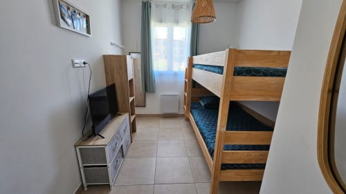 Chambre moderne à la Résidence Marina di Bravone à Linguizzetta avec lits superposés, TV et porte-fenêtre donnant sur la mer