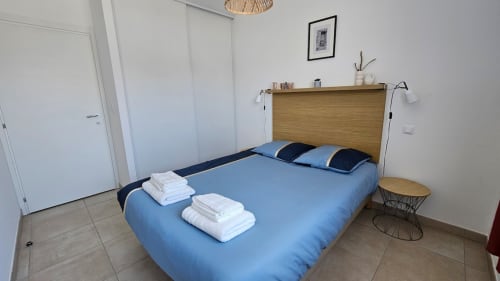 Chambre moderne à la Résidence Marina di Bravone avec lit bleu, tête de lit en bois et serviettes blanches à Linguizzetta