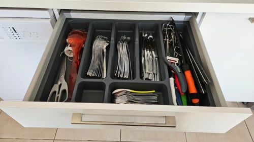 Tiroir de cuisine ouvert à la Résidence Marina di Bravone présentant couverts, ustensiles et outils de cuisine organisés dans des compartiments