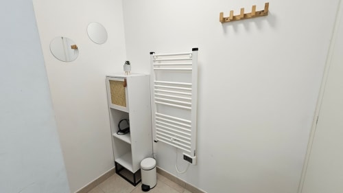 Coin salle de bains minimaliste à la Résidence Marina di Bravone avec sèche-serviettes chauffant blanc, meuble de rangement et miroirs ronds
