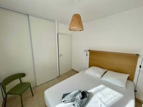 Modern bedroom at Résidence Marina di Bravone with wooden bed, woven pendant lamp, and green chair in Linguizzetta, France