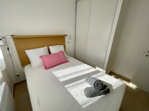 Bright bedroom at Résidence Marina di Bravone with wooden headboard, white bedding, pink pillow, and rolled towels in