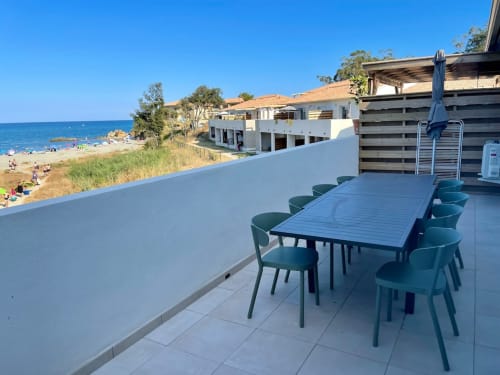 Waterfront terrace at Résidence Marina di Bravone with dining table, teal chairs, and Mediterranean Sea view in Linguizzetta,