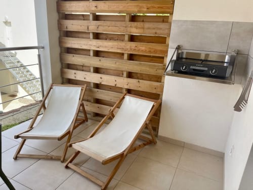 Two wooden beach chairs with white cushions on a patio at Résidence Marina di Bravone, with wooden privacy screen and grill