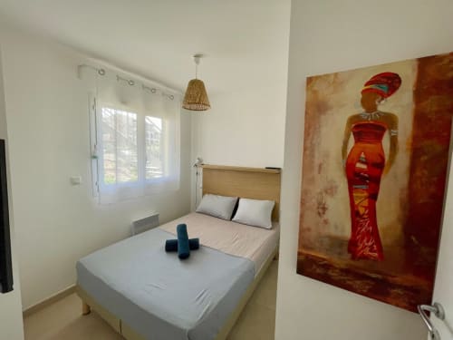 Bright bedroom at Résidence Marina di Bravone with double bed, wicker pendant light, and African-inspired wall art in