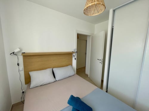 Bright modern bedroom at Résidence Marina di Bravone with wooden headboard, white bedding, and en-suite bathroom entry