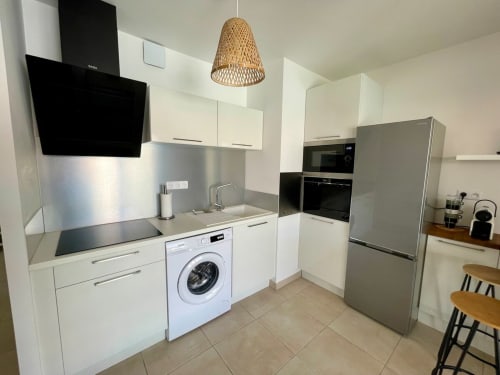 Modern kitchen in Marina di Bravone apartment with white cabinets, stainless steel appliances, and woven pendant light