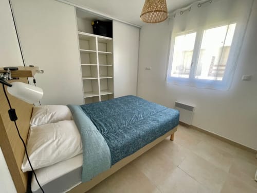 Camera moderna presso Résidence Marina di Bravone con copriletto blu, mobili in legno, armadio bianco e finestre luminose