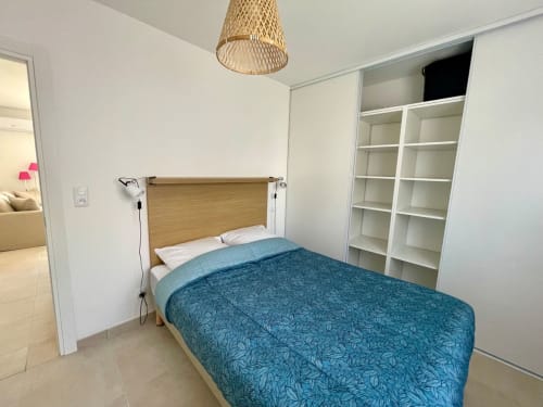 Camera luminosa presso Résidence Marina di Bravone a Linguizzetta con letto in legno, biancheria turchese, scaffali bianchi e tessuti intrecciati