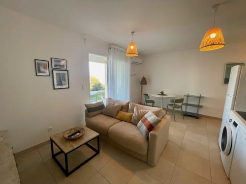 Appartement moderne à la Résidence Marina di Bravone avec canapé beige, salle à manger et vue sur l'océan par portes vitrées