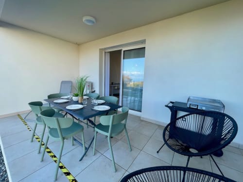 Balcon de l'appartement en front de mer Marina di Bravone avec table à manger, chaises menthe, barbecue et vue sur la mer à Linguizzetta