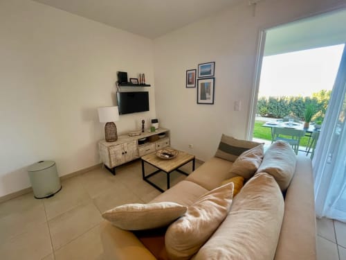 Salon moderne de la Résidence Marina di Bravone avec canapé beige, téléviseur et terrasse surplombant la piscine du jardin