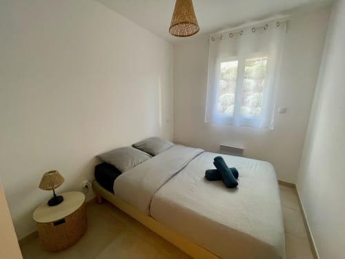 Chambre moderne à la Résidence Marina di Bravone avec lit queen-size, lampadaire en rotin et vue sur le jardin