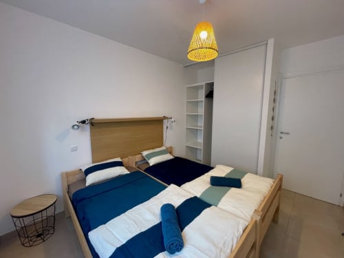 Chambre lumineuse à la Résidence Marina di Bravone avec deux lits, tête de lit en bois, suspension jaune et rangements blancs