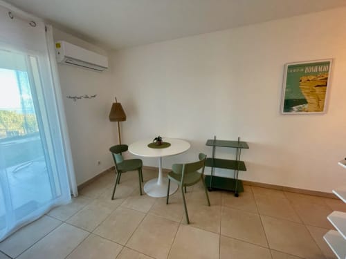 Séjour lumineux avec table ronde blanche, chaises vertes et étagères à l'hôtel Marina di Bravone à Linguizzetta