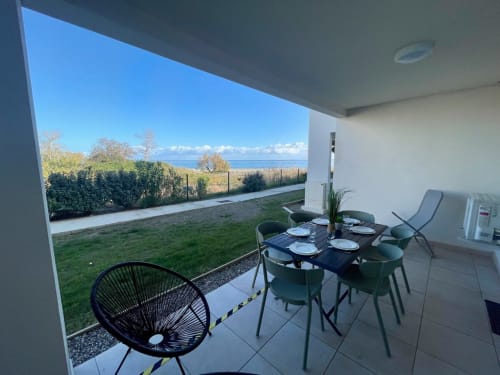 Patio moderne de la Résidence Marina di Bravone avec table à manger, transats, jardin et vue sur la mer en Corse