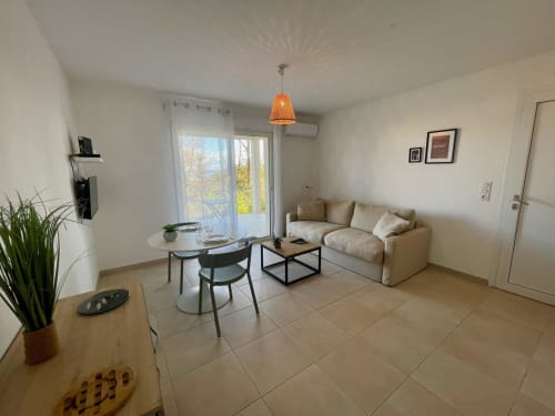 Studio moderne à la Résidence Marina di Bravone avec vue mer, canapé beige, table à manger et lampe suspendue orange