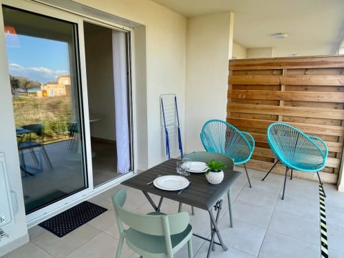Balcon du studio à la Résidence Marina di Bravone avec chaises turquoise, table à manger et vue sur mer