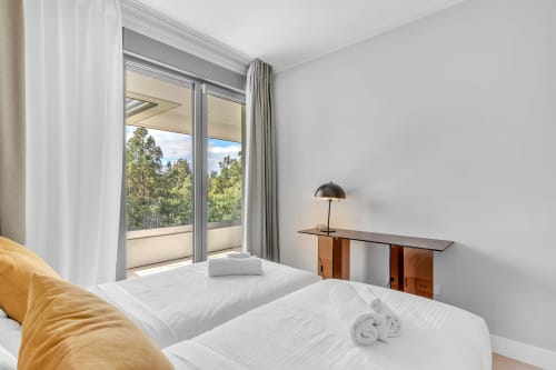 Jasna sypialnia w apartamencie HomyMarbella w Elvirii z balkonem z widokiem na ogród, białą pościelą, drewnianym biurkiem i naturalnym światłem