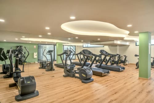 Nowoczesna sala fitness w apartamencie HomyMarbella w Elvirizie z urządzeniami kardio, drewnianymi podłogami i zielonymi ścianami akcentowymi