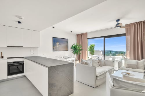 Nowoczesny apartament otwartej przestrzeni w HomyMarbella Elviria z widokiem na morze, białą kuchnią, szarą wyspą i beżowymi meblikami
