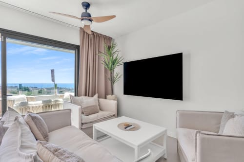 Nowoczesny salon apartamentu z widokiem na morze w HomyMarbella, Marbella – telewizor, wentylator sufitowy, balkon z panoramą wybrzeża