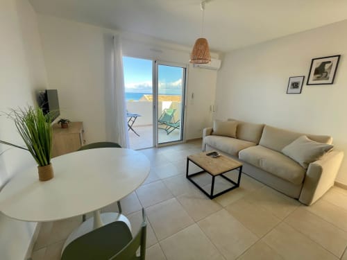 Monolocale con vista mare a Marina di Bravone, Corsica con divano beige, tavolo da pranzo e accesso alla terrazza
