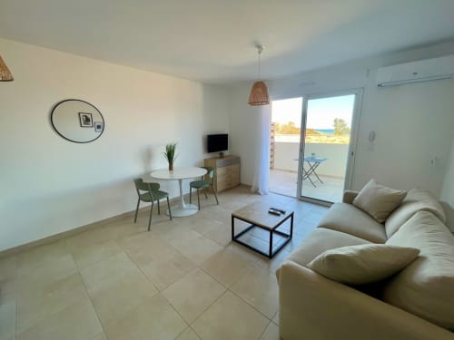 Moderno monolocale a Résidence Marina di Bravone con divano beige, tavolo da pranzo e terrazza con vista sul mare a Linguizzetta