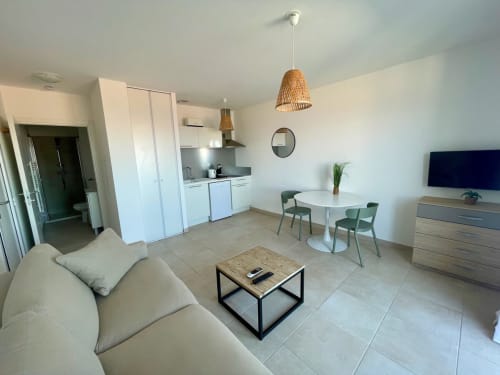 Moderno monolocale a Marina di Bravone con angolo cottura, zona pranzo, divano beige e lampada a sospensione intrecciata