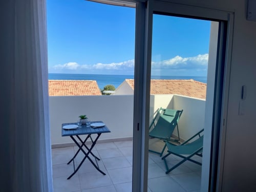 Balcone di studio alla Résidence Marina di Bravone con vista mare, tavolo da pranzo, sdraio e tetti costieri.