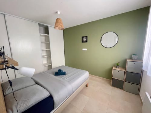 Chambre moderne à la Résidence Marina di Bravone avec mur d'accent vert olive, lit, rangements et luminaires suspendus